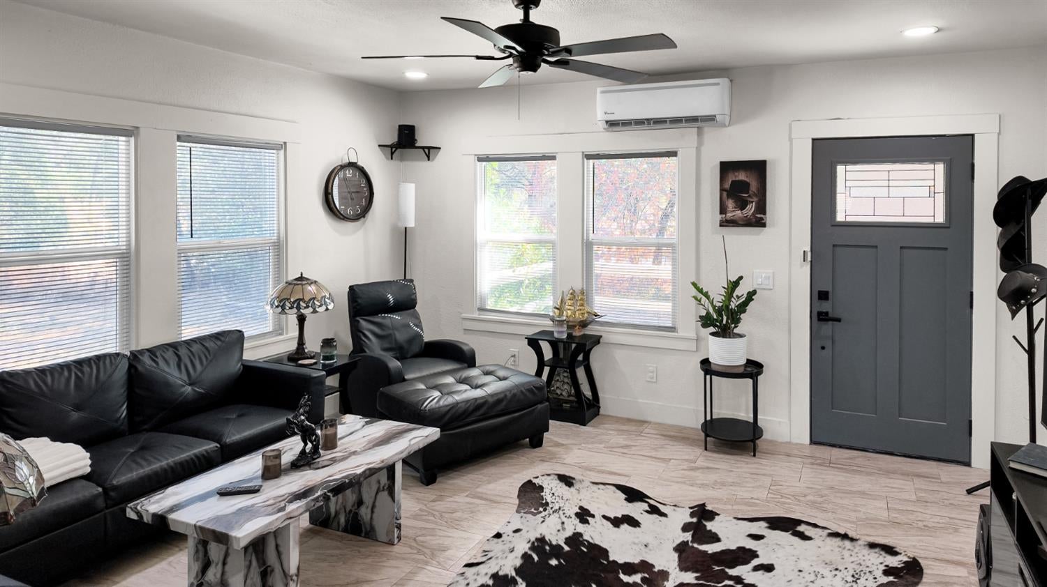 Furnished living room with black leather seating, a cowhide rug, and a gray entry door.