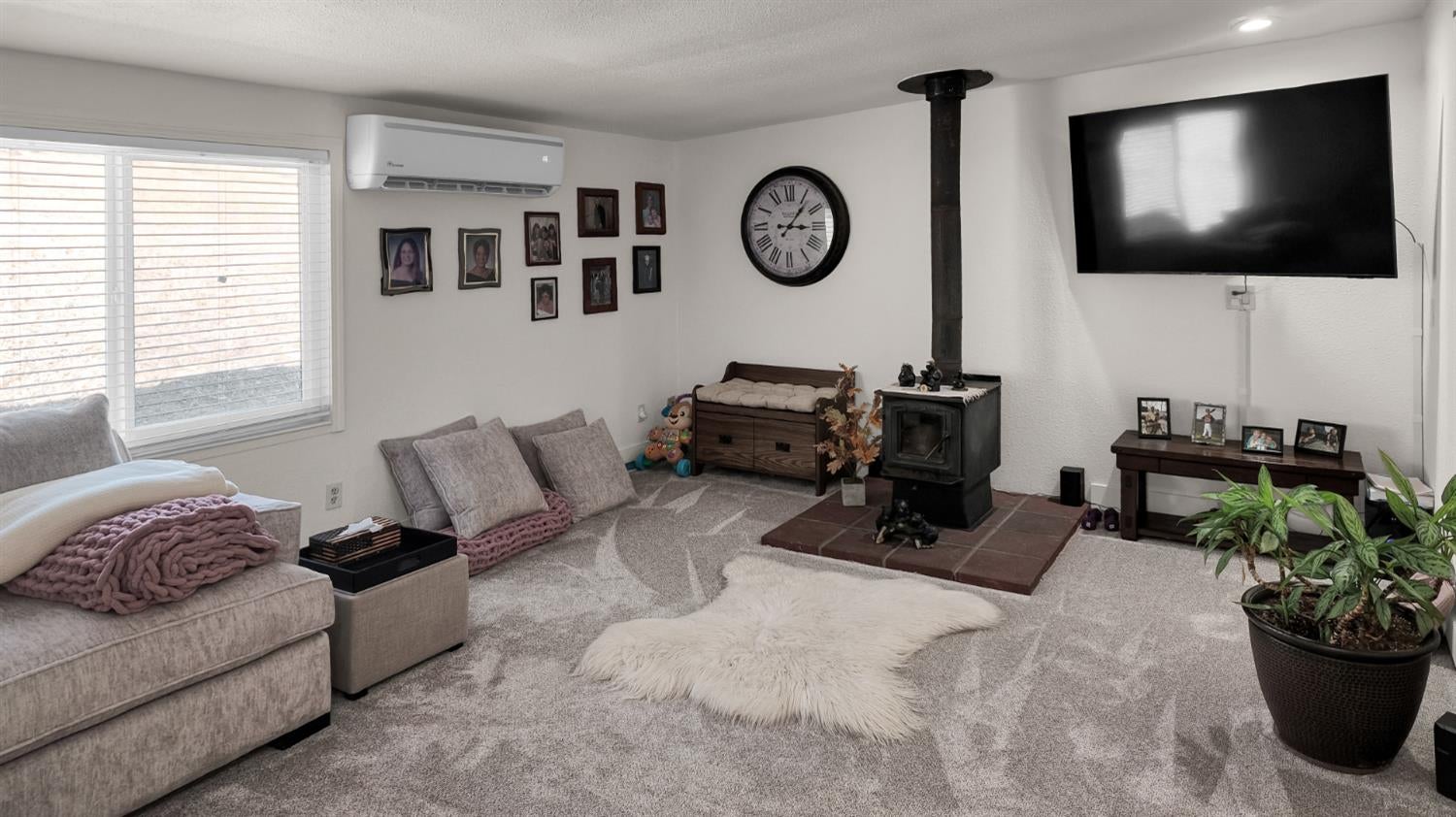 Living room with a black wood stove, brick hearth, gray carpet, and wall-mounted television.