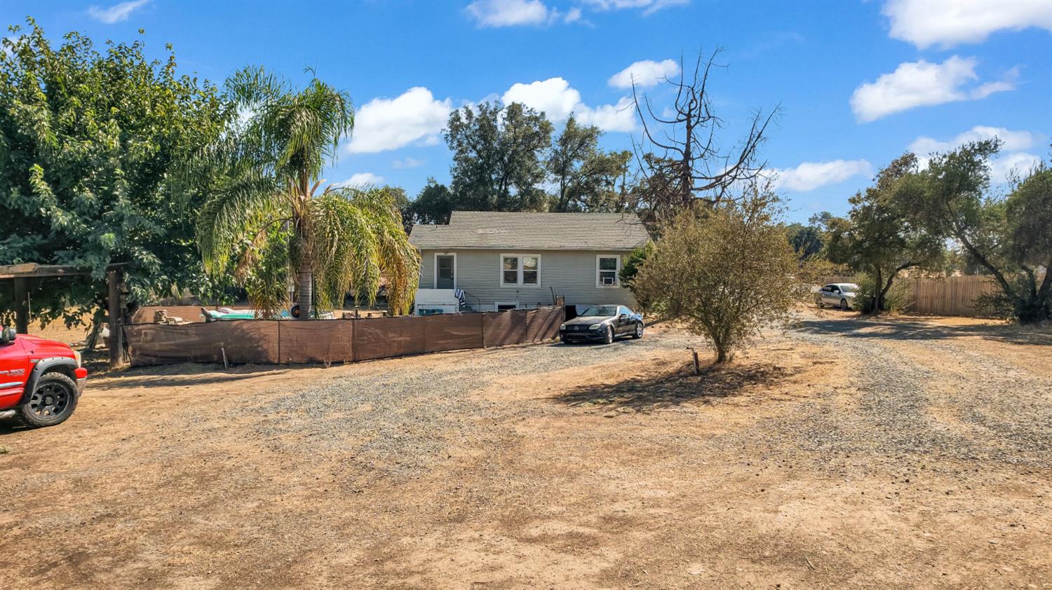 Single-story house beyond a broad dry yard, with palms and a fenced pool area.
