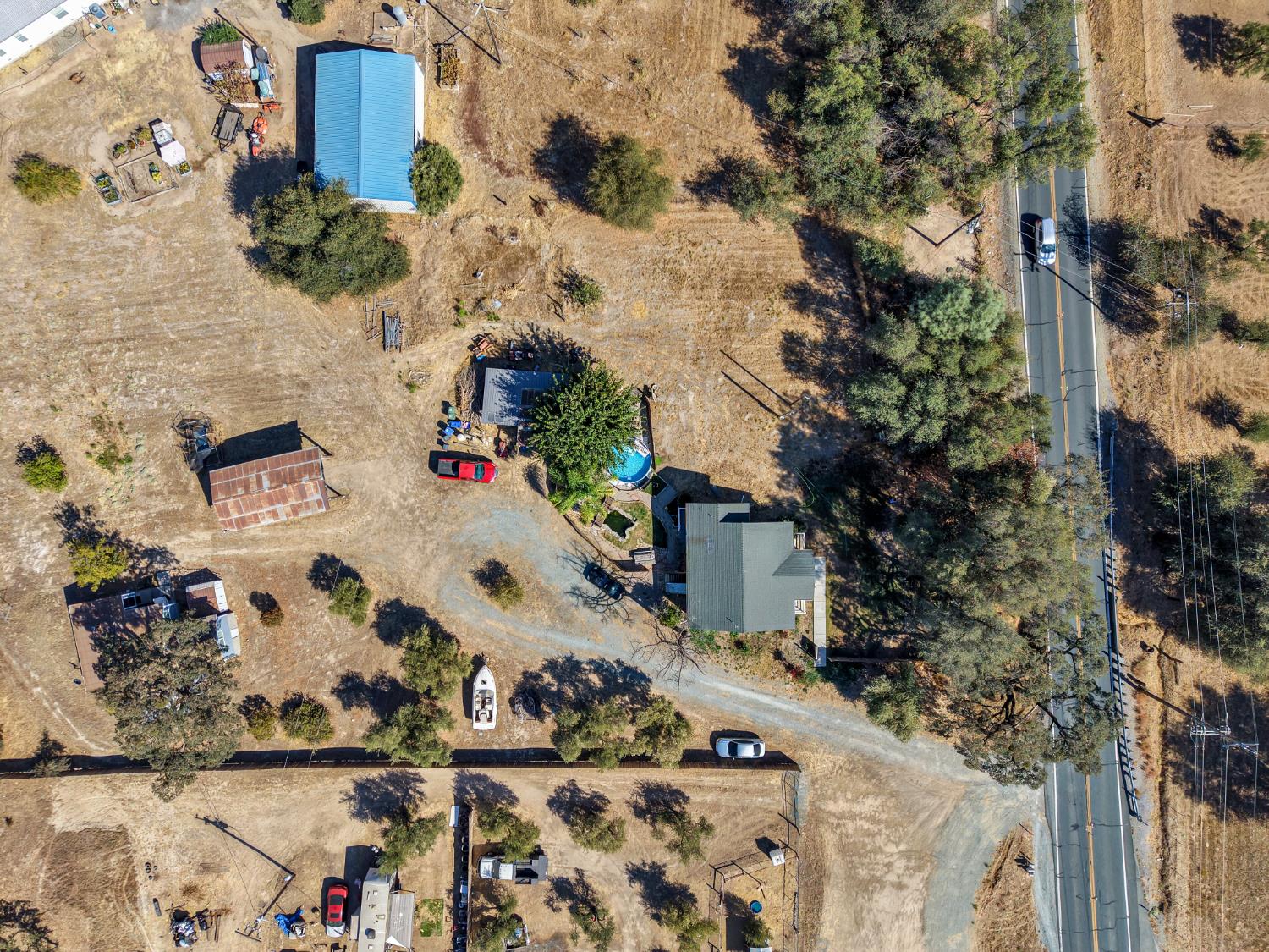 Aerial view of a rural property with a house, outbuildings, and a swimming pool beside a highway.