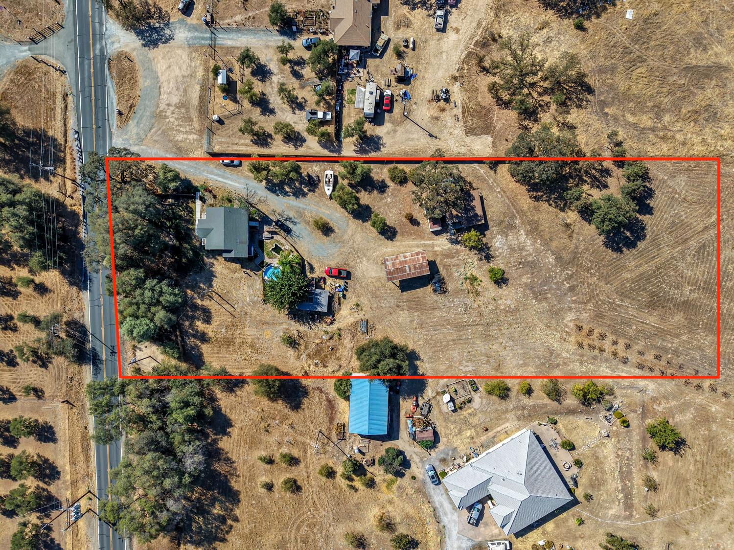 Aerial view of a rural property outlined in red, with a house, outbuildings, and open land.