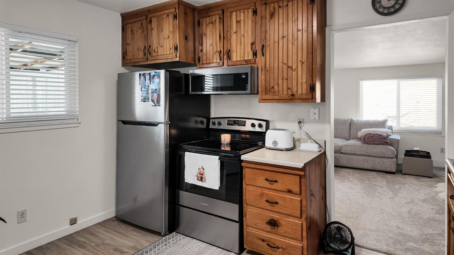 Kitchen with knotty-pine cabinets and stainless appliances, opening to a living room with a gray sofa.