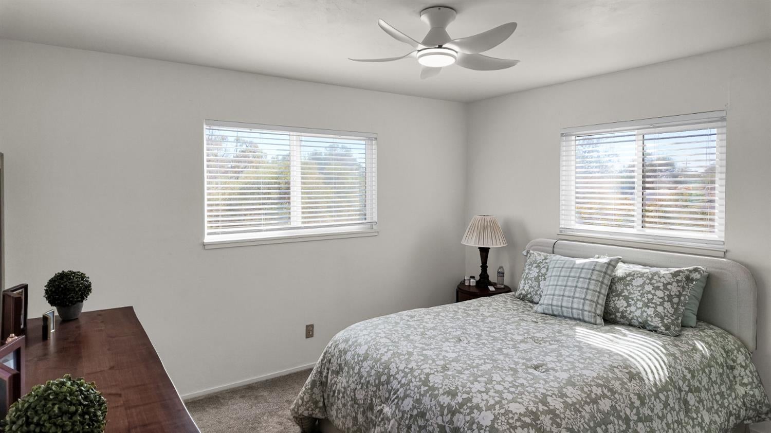 Bedroom with a floral quilted bed, two bright windows, and a ceiling fan.