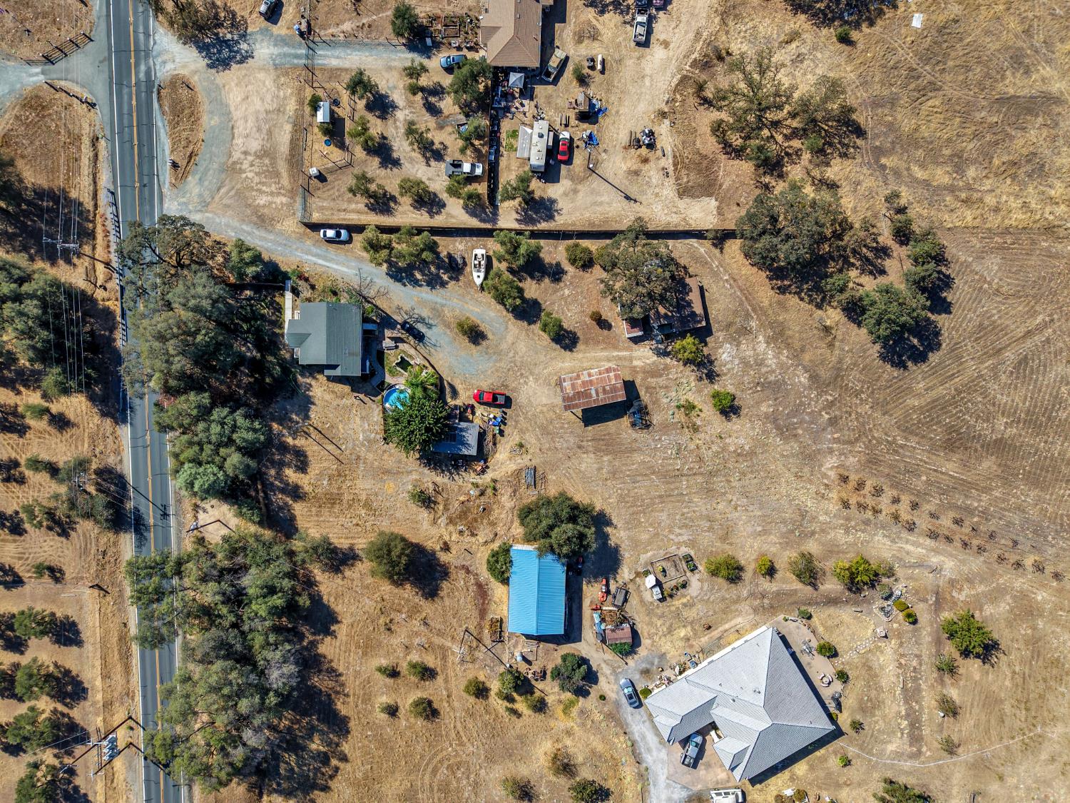 Aerial view of a rural property with several buildings and dry open land beside a highway.