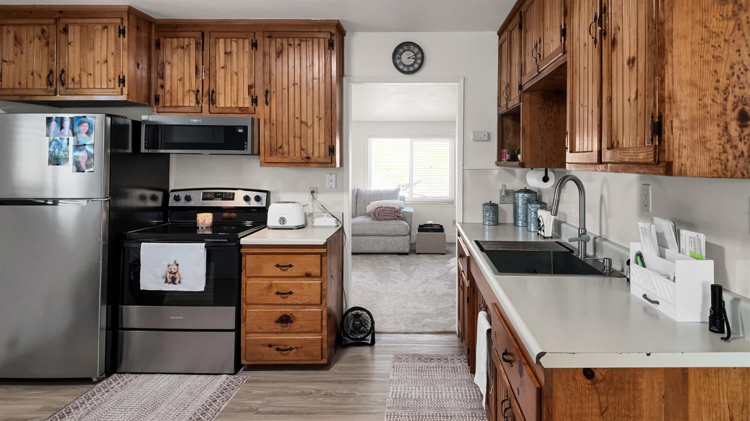 Kitchen with knotty wood cabinets, white counters, black sink, and stainless steel refrigerator and range.