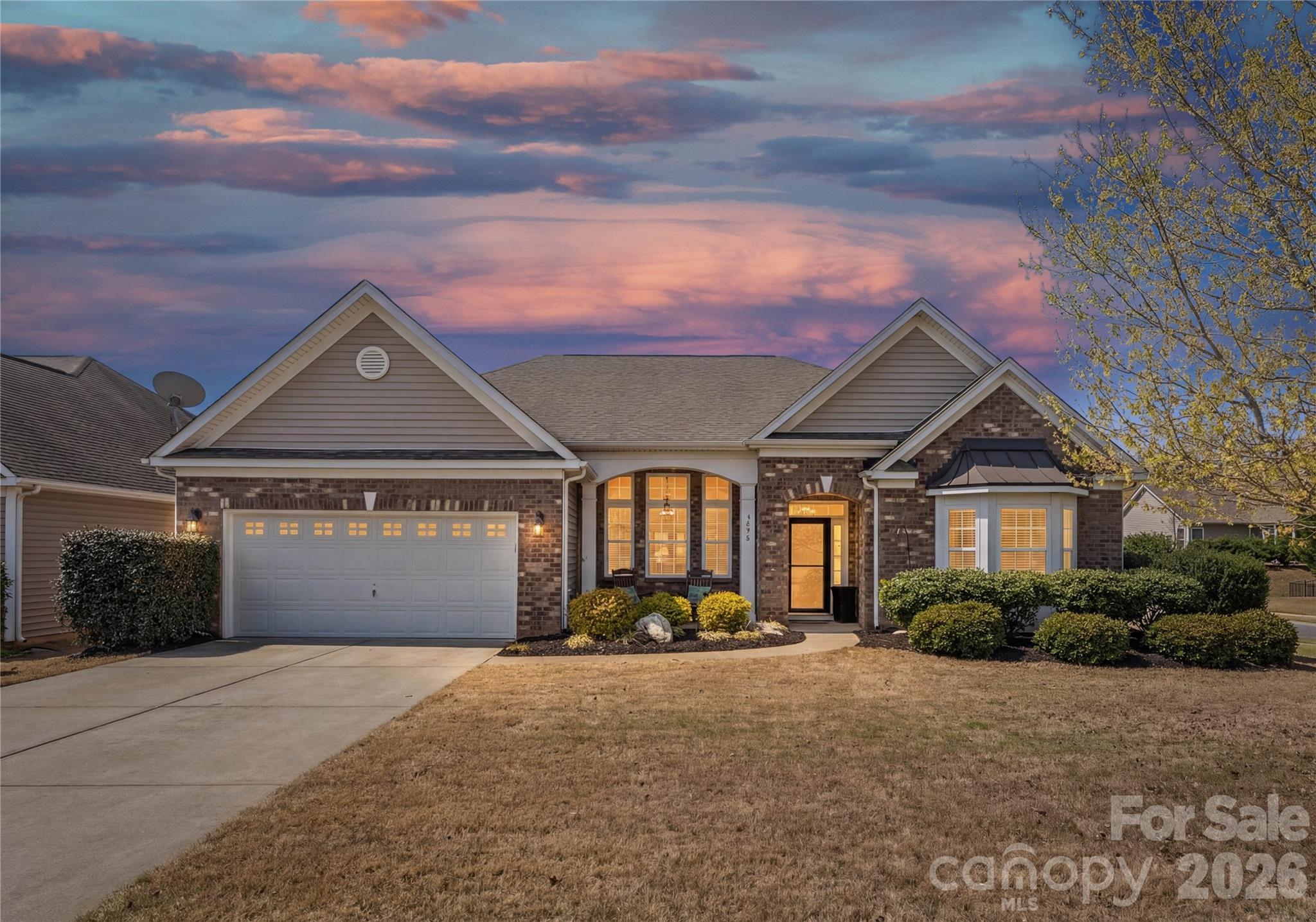 Single-story brick home with a two-car garage and warmly lit windows at dusk.