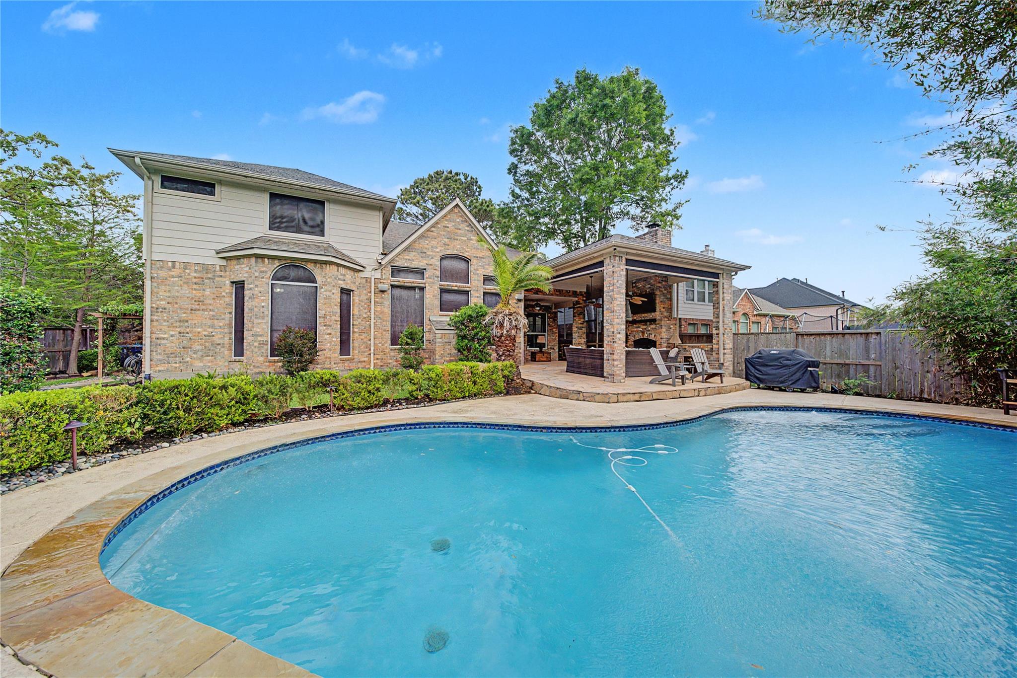 Two-story home behind a curved swimming pool, with a covered brick patio and outdoor seating.
