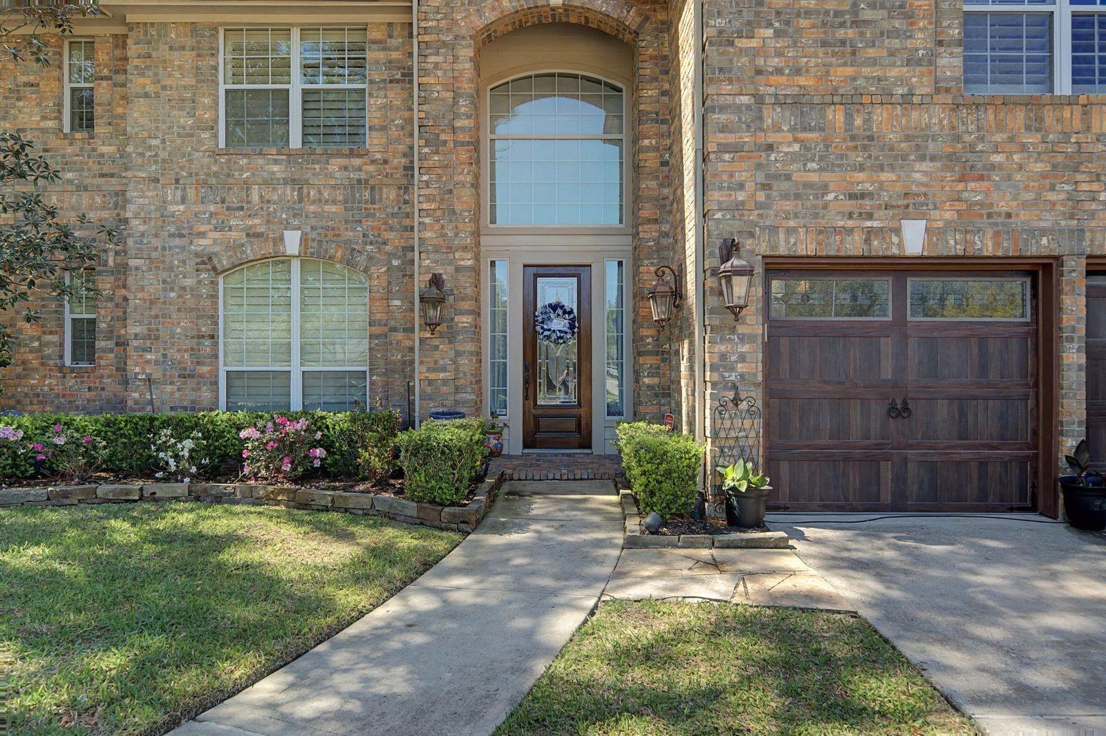 Brick home exterior with an arched entry, dark wood garage door, and landscaped front walkway.