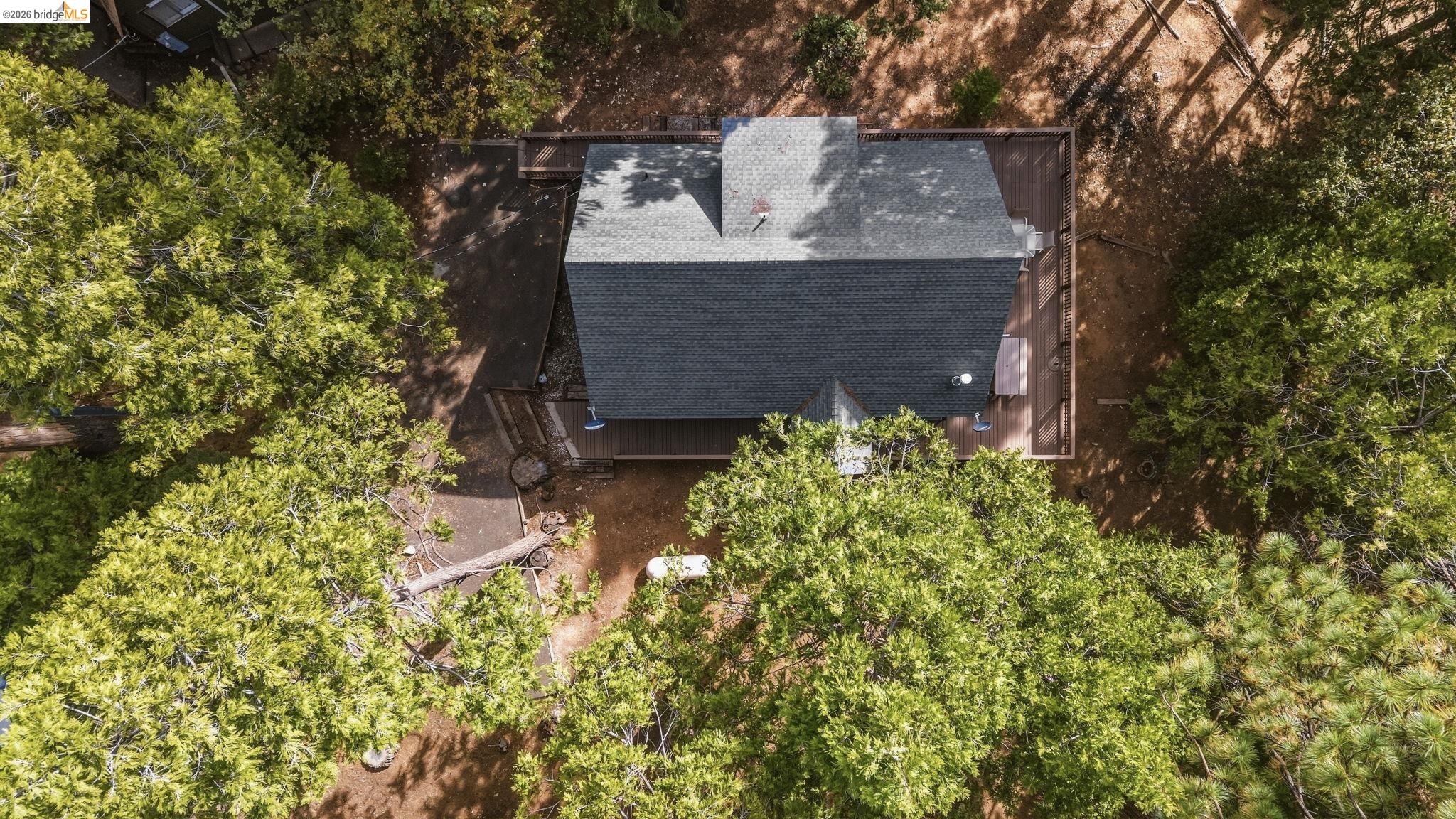 Aerial view of a gray-roofed house surrounded by dense trees, with a wooden deck around the home.