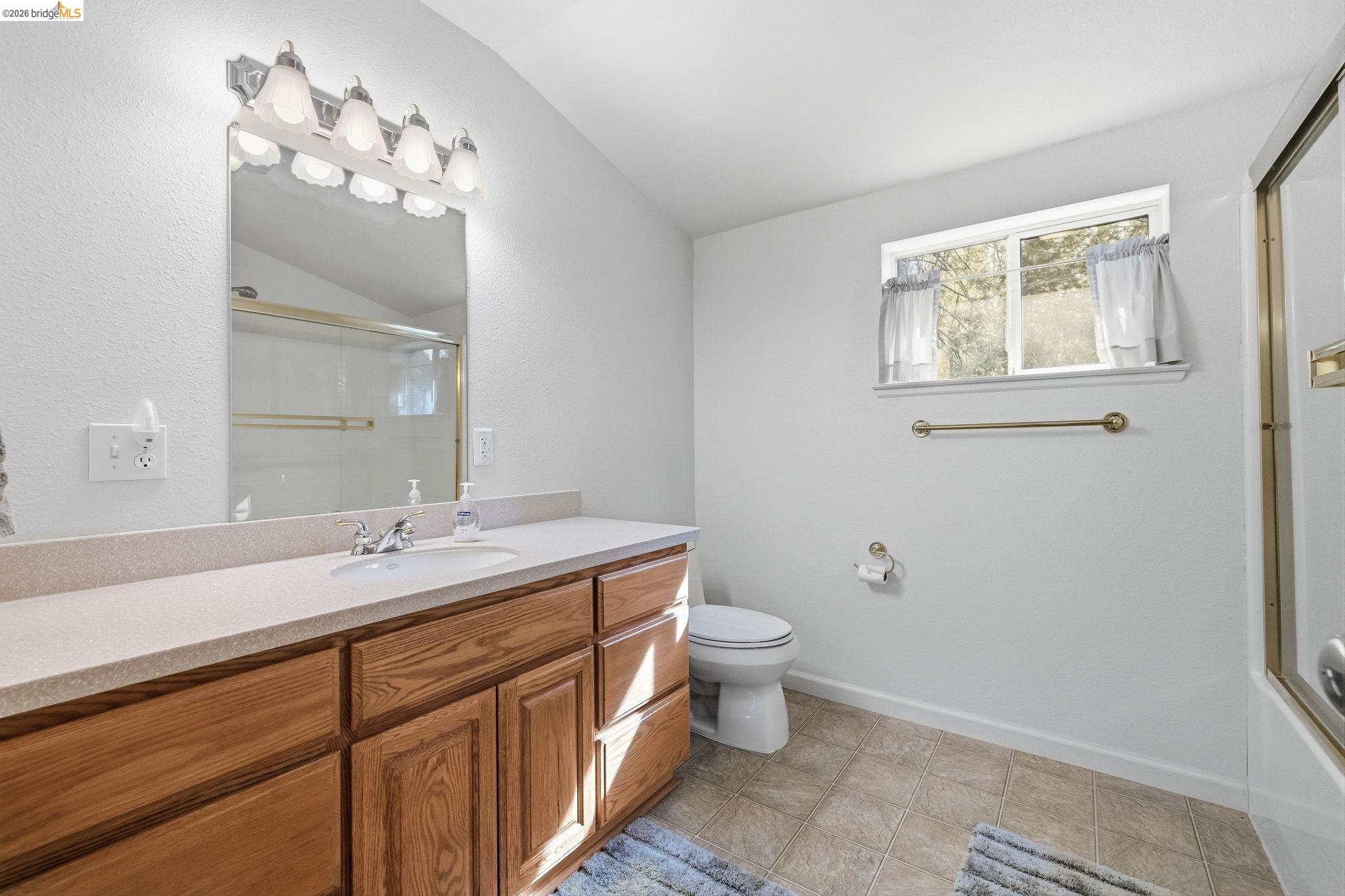 Bathroom with a long wood vanity, large mirror, curtained window, and glass shower.