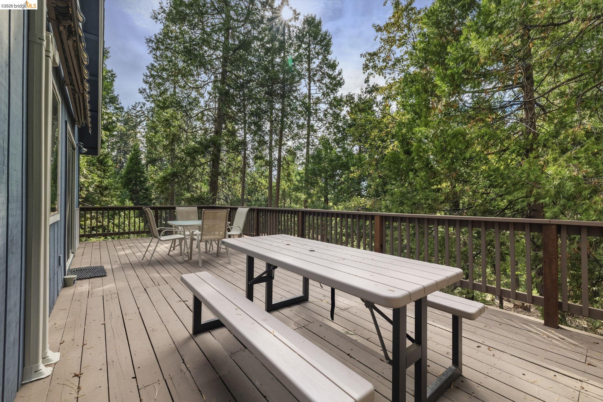 Wooden deck with picnic table and dining set surrounded by trees.