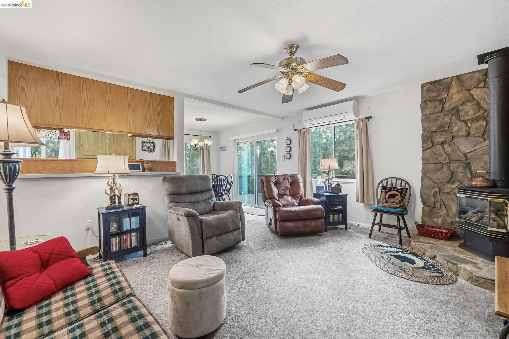 Furnished living room with stone fireplace, wood stove, and sliding glass doors to trees.
