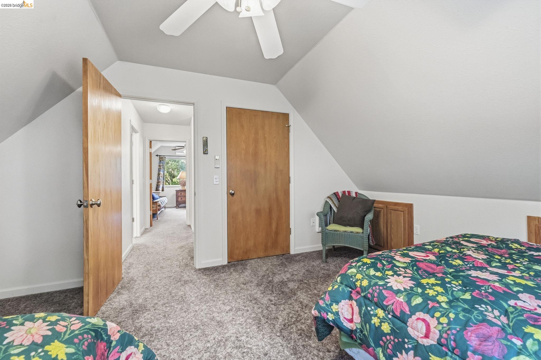 Furnished bedroom with a sloped ceiling, floral bedspreads, and an open door to the hallway.