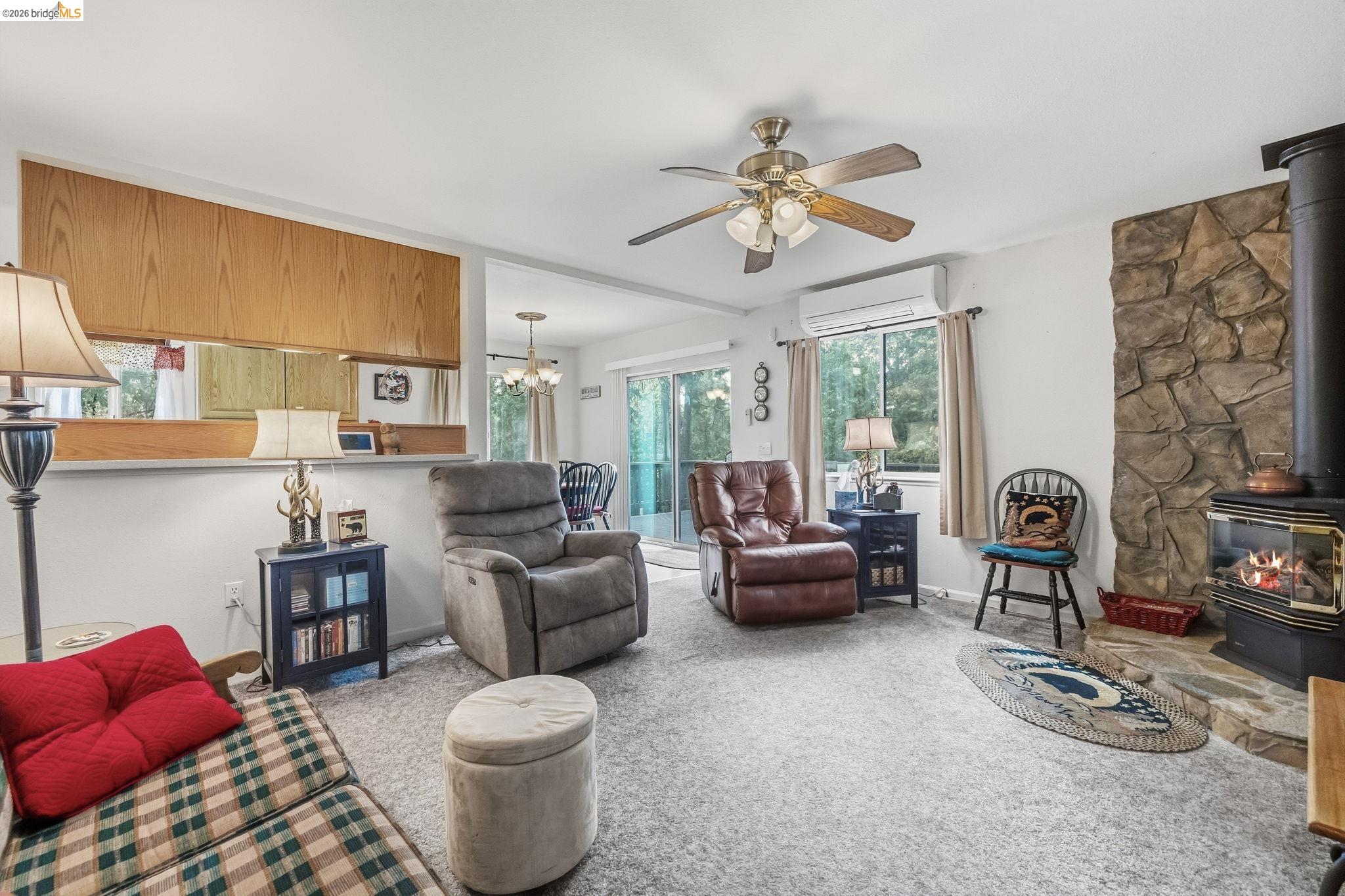 Living room with a stone fireplace and wood stove, recliners, and sliding glass doors.