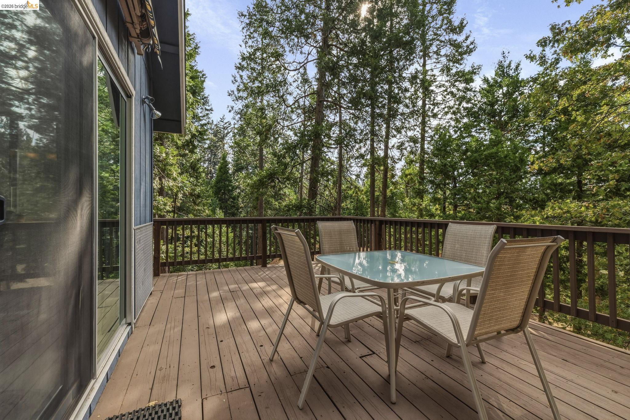 Wooden deck with outdoor dining set overlooking tall trees.