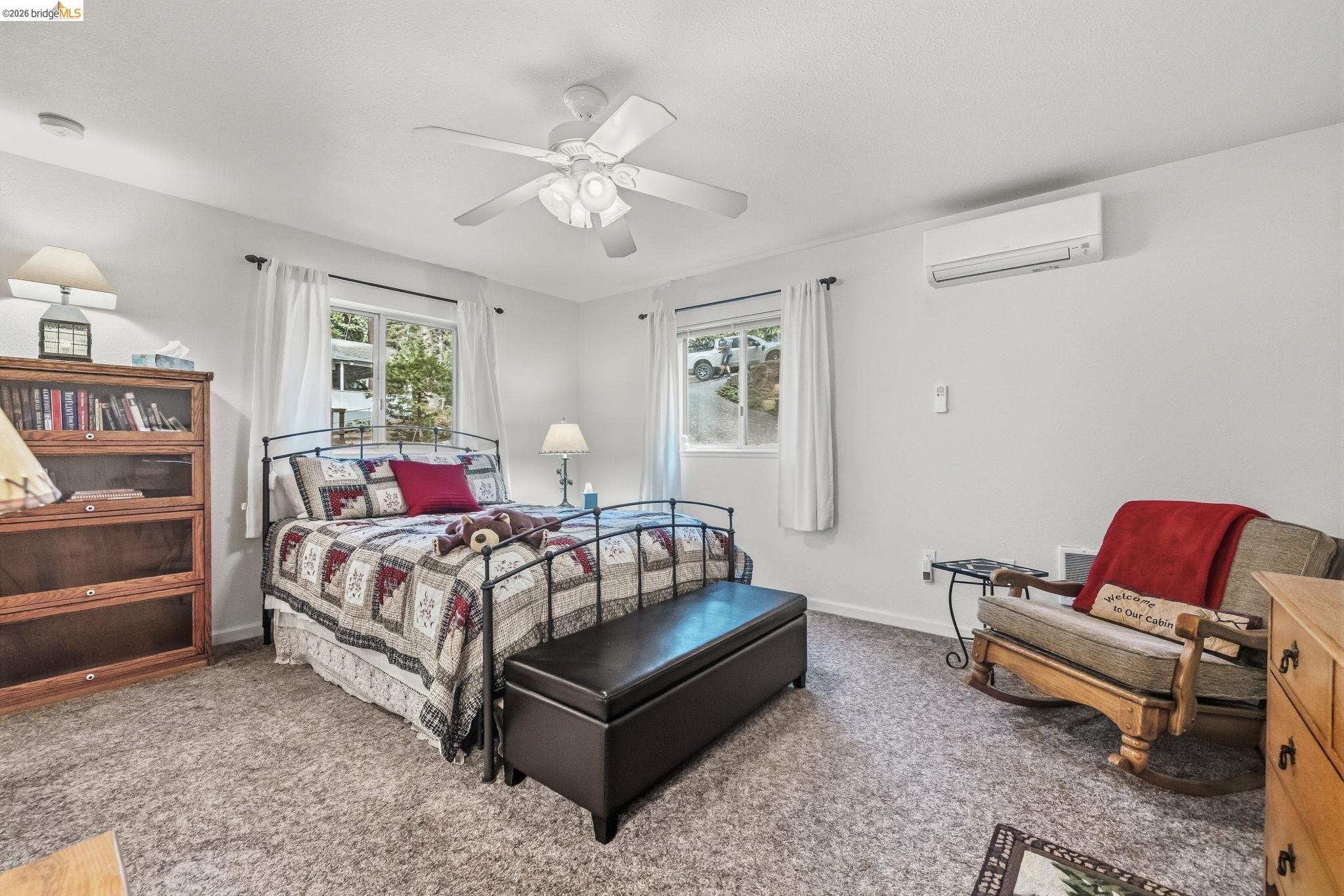 Furnished bedroom with a patchwork-quilt bed, dark storage bench, bookcase, and cushioned wooden chair.