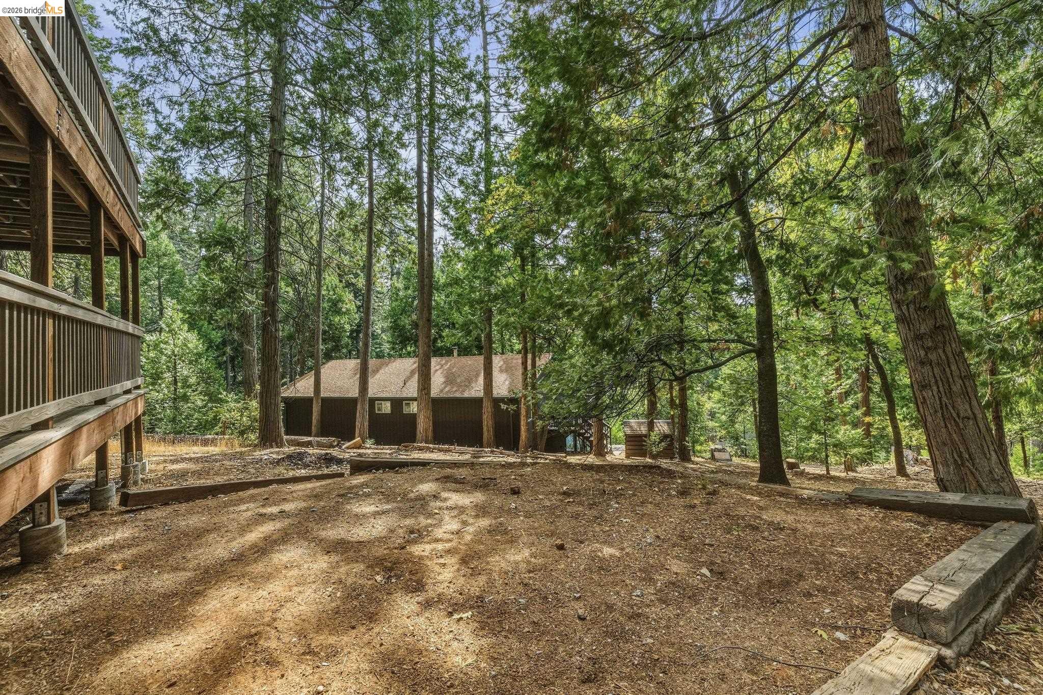 Wooded cabin property with a raised wooden deck and a shaded, leaf-covered yard.