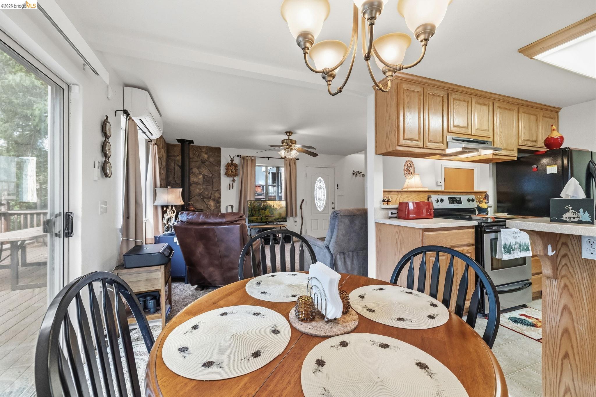 Open-plan dining area and kitchen with a round wooden table, wood cabinets, and a stone fireplace wall.