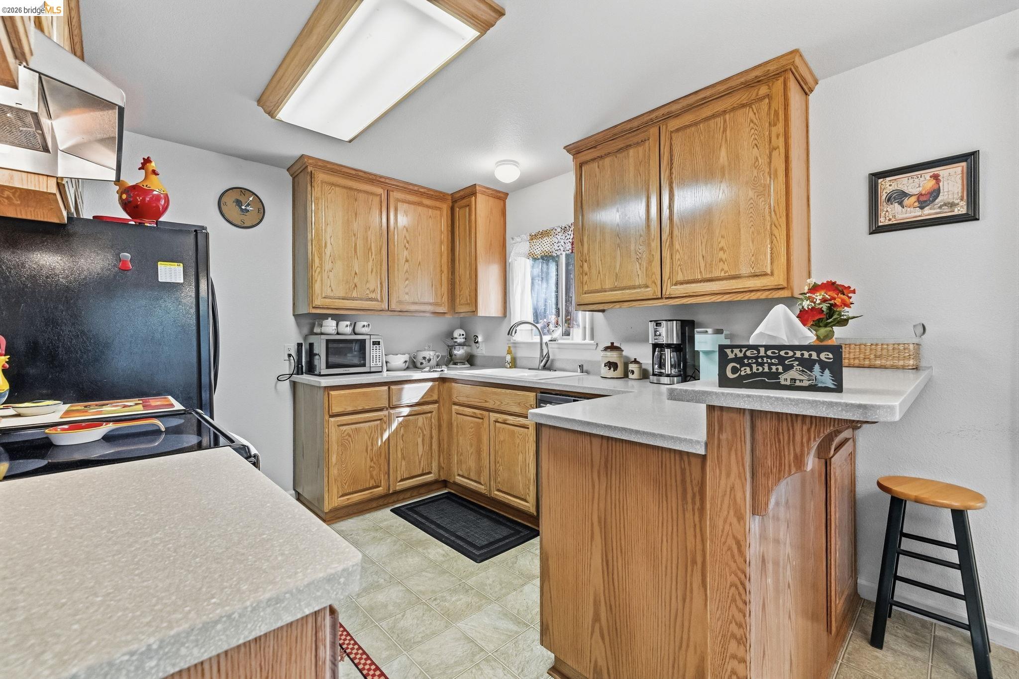 Kitchen with honey-colored wood cabinets, light countertops, and a raised breakfast bar with a stool.
