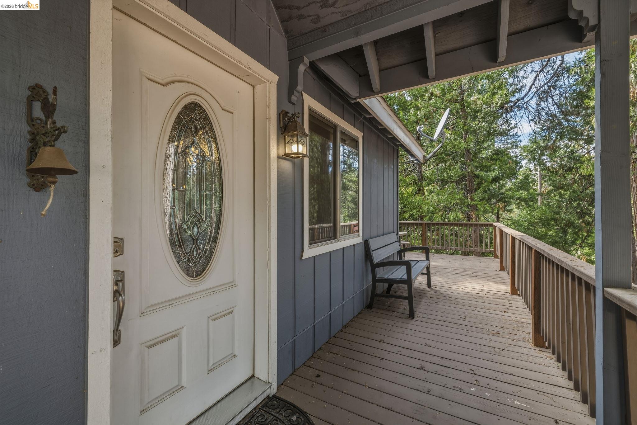 Covered wooden entry porch with a decorative glass door, bench, and wooded surroundings.