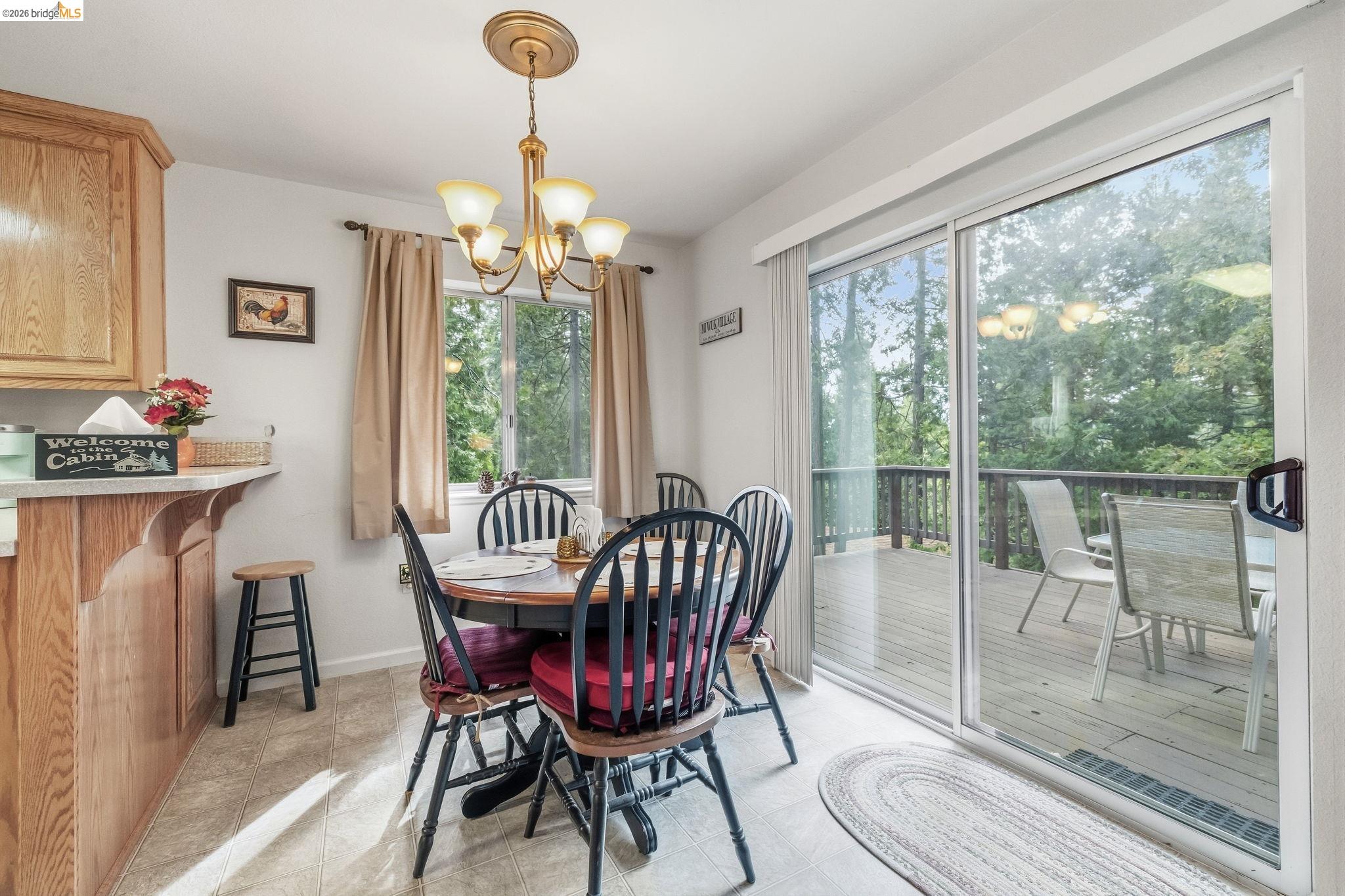 Dining area with a round table beside sliding glass doors opening onto a wooded deck.