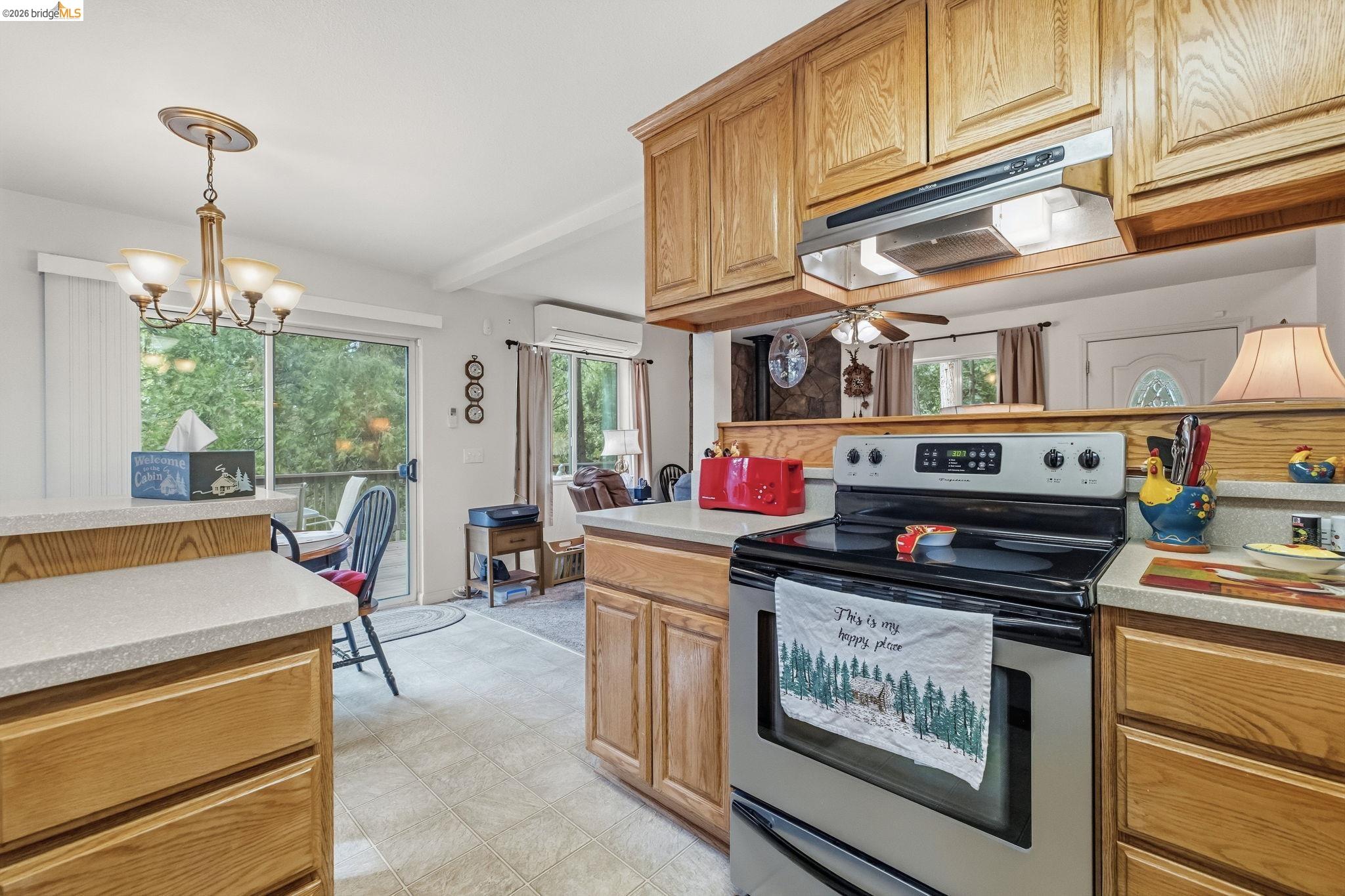 Kitchen with honey-colored wood cabinets, a peninsula, and sliding glass doors overlooking trees.