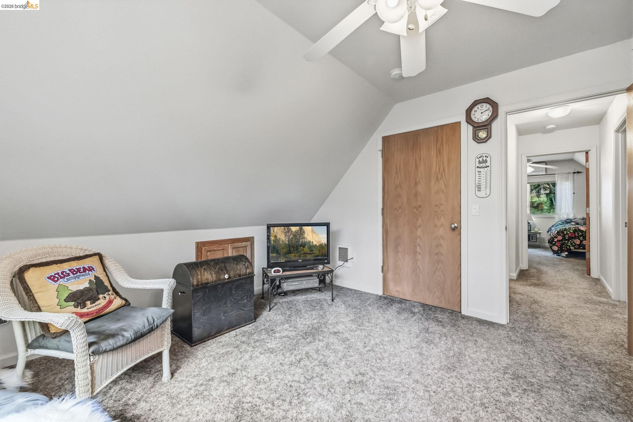 Upstairs sitting area with a sloped ceiling, wicker chair, wooden chest, and doorway to a bedroom.