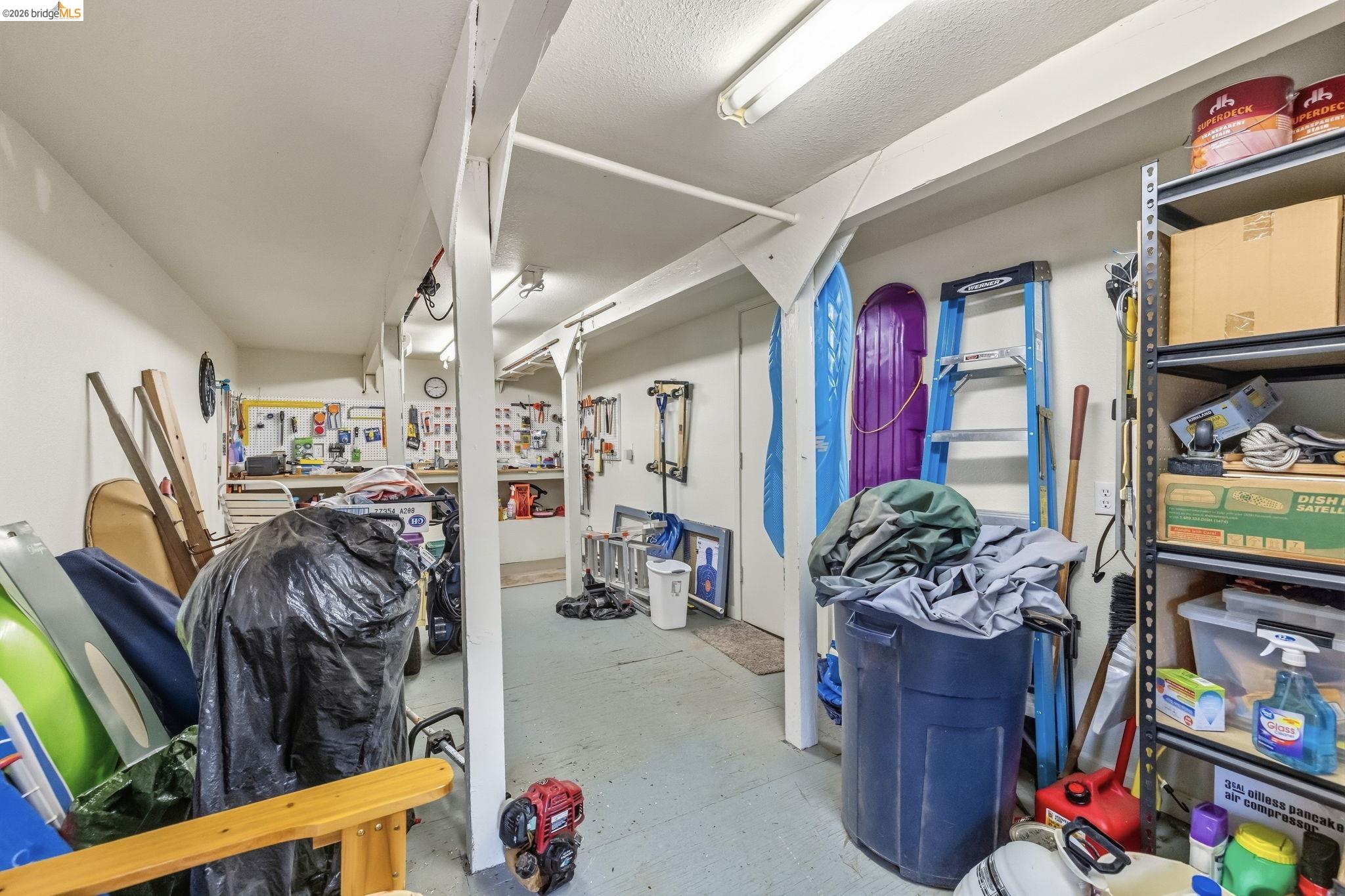 Workshop and storage room with tool-covered workbenches, ladders, sleds, and packed shelving.