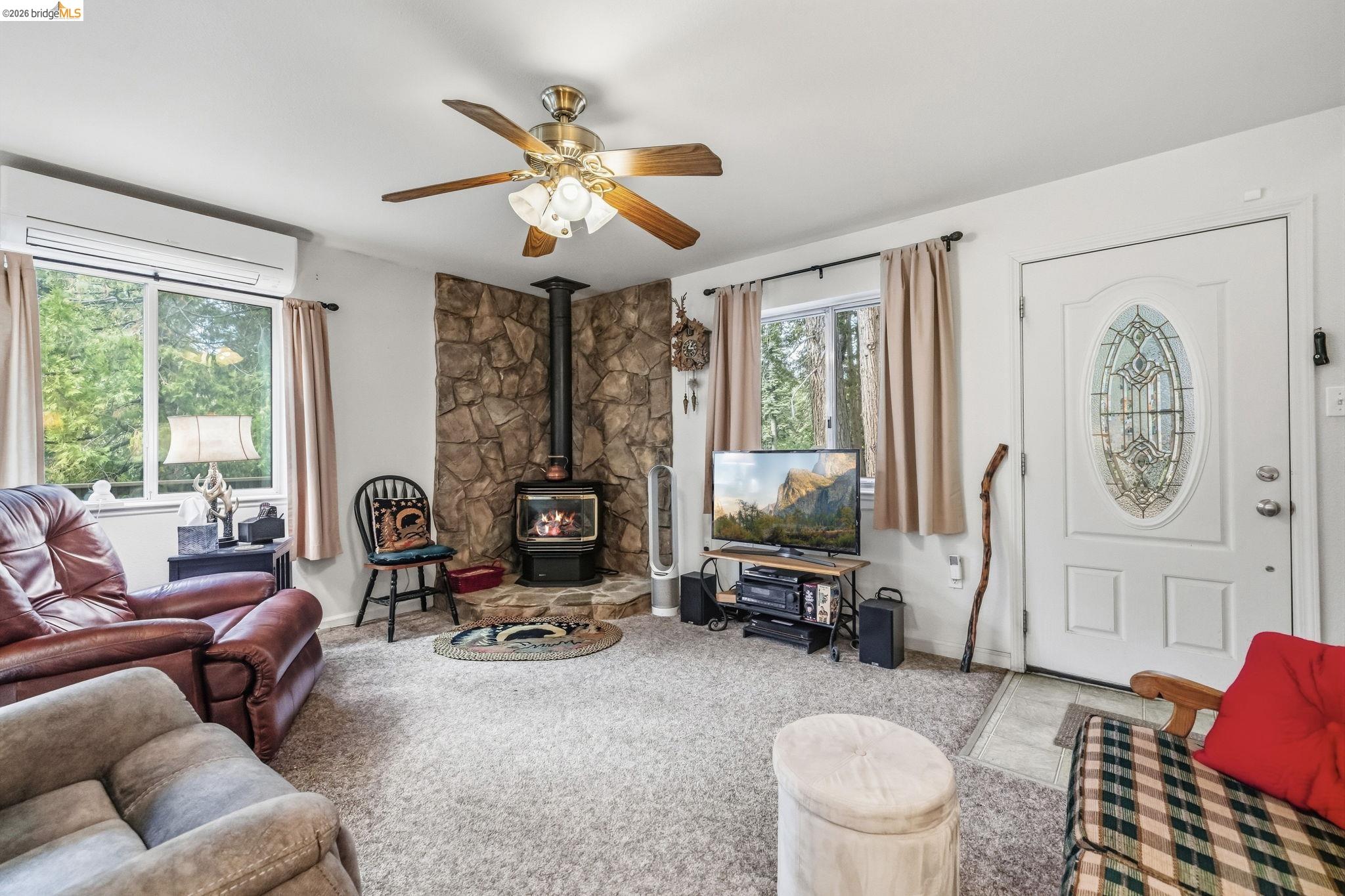 Living room with a stone fireplace and wood-burning stove, leather seating, and windows overlooking trees.