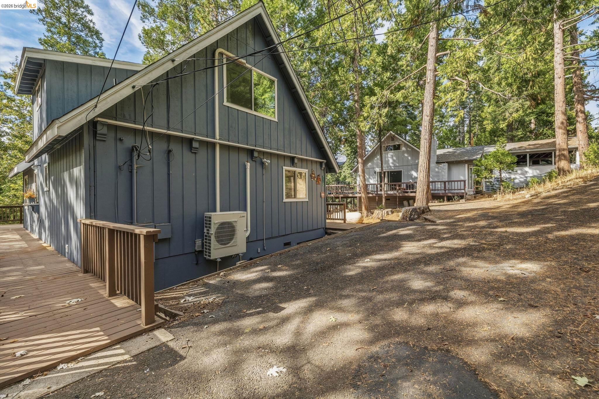 Dark gray gabled home with a wooden deck among tall pine trees.
