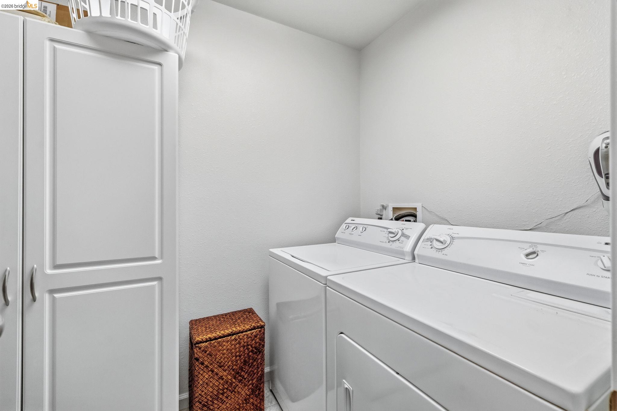 Laundry room with a top-load washer and dryer beside a tall white storage cabinet.