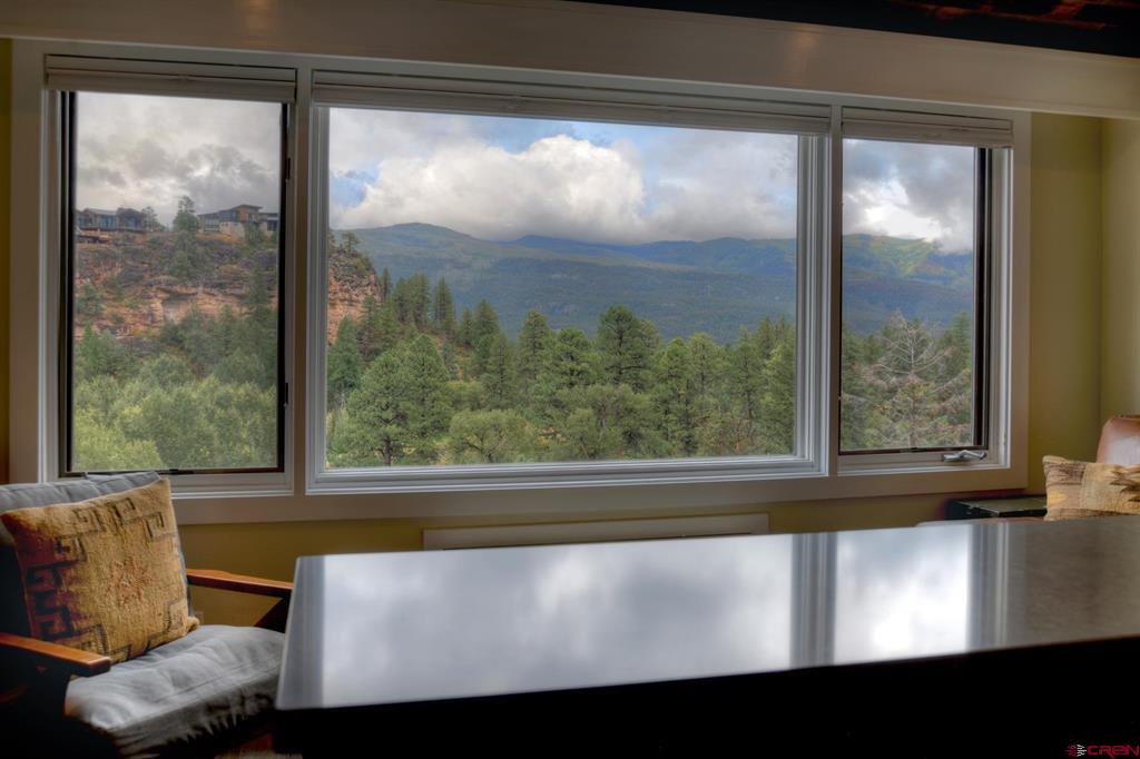 Dining area with a reflective table and wide windows overlooking pine-covered hills and distant mountains.