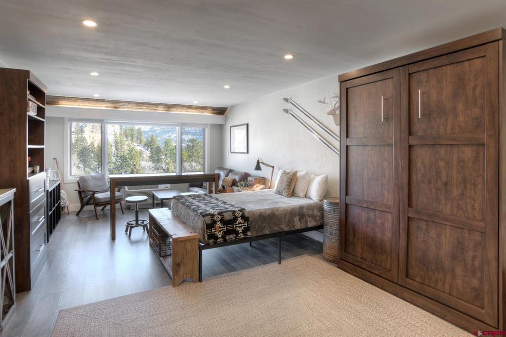 Furnished bedroom with a king bed, large wooden closet, and mountain views through wide windows.