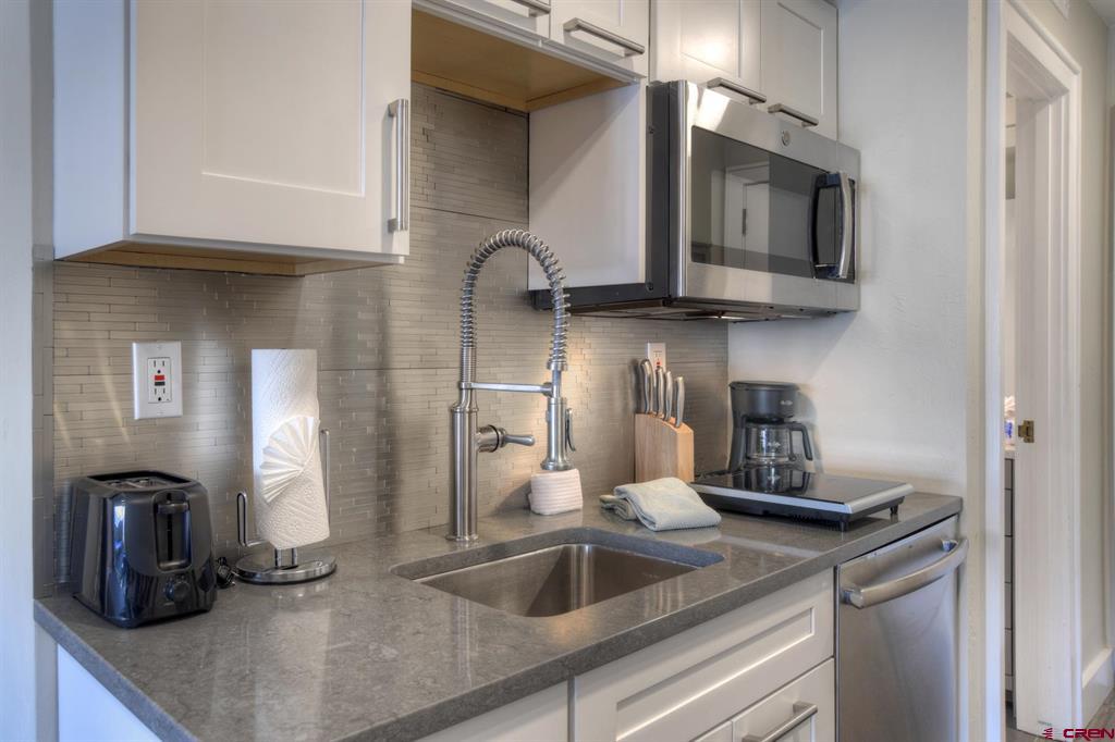 Modern kitchen with white cabinets, gray countertops, and a tall spring-coil faucet over the sink.
