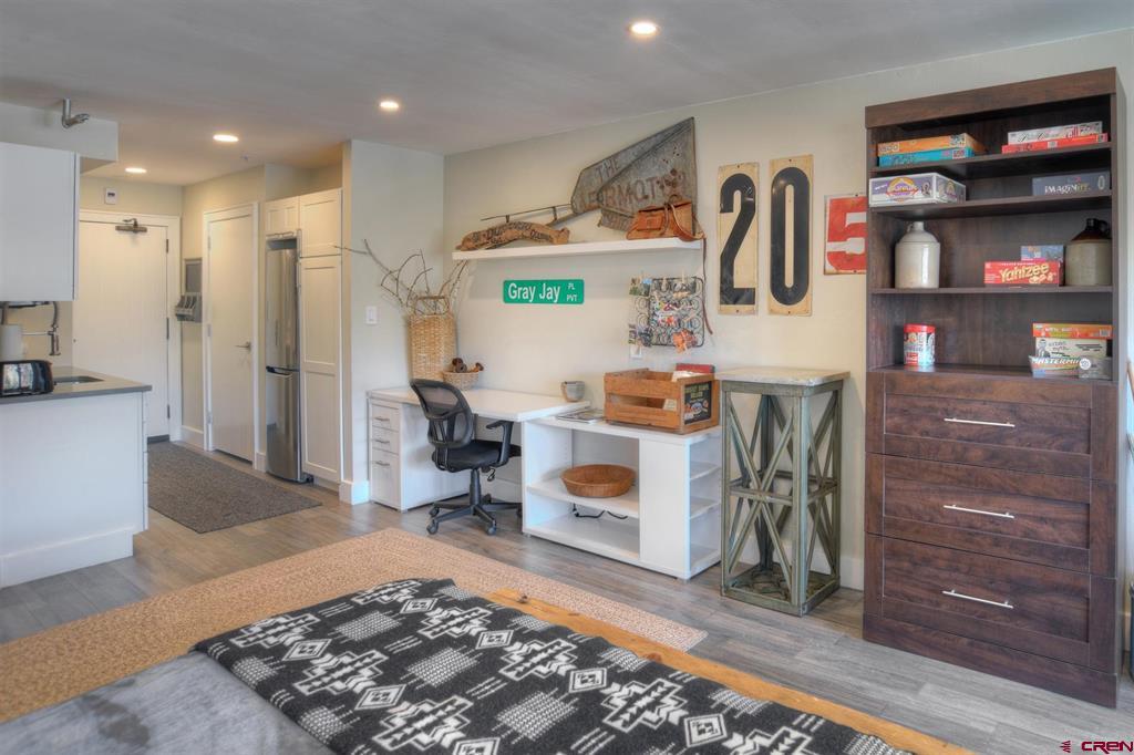Bedroom with a bed, desk nook, dark wood shelving, and kitchenette.