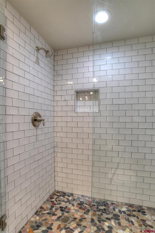 Walk-in shower with white subway tile, a built-in niche, and a colorful pebble floor.