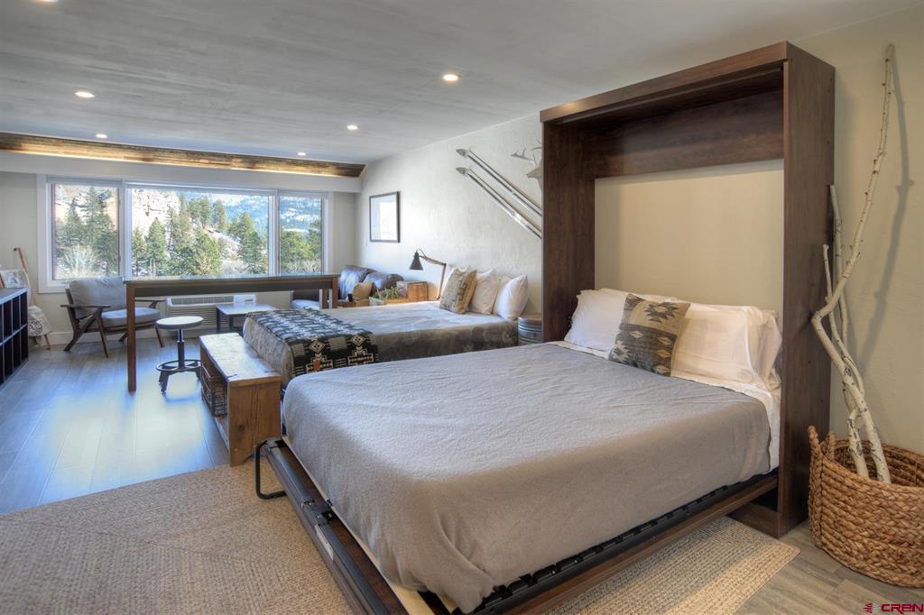 Furnished bedroom with two beds and wide windows overlooking trees and mountains.
