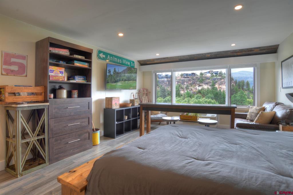 Bedroom with a large bed and wide window overlooking a rocky, tree-covered hillside.