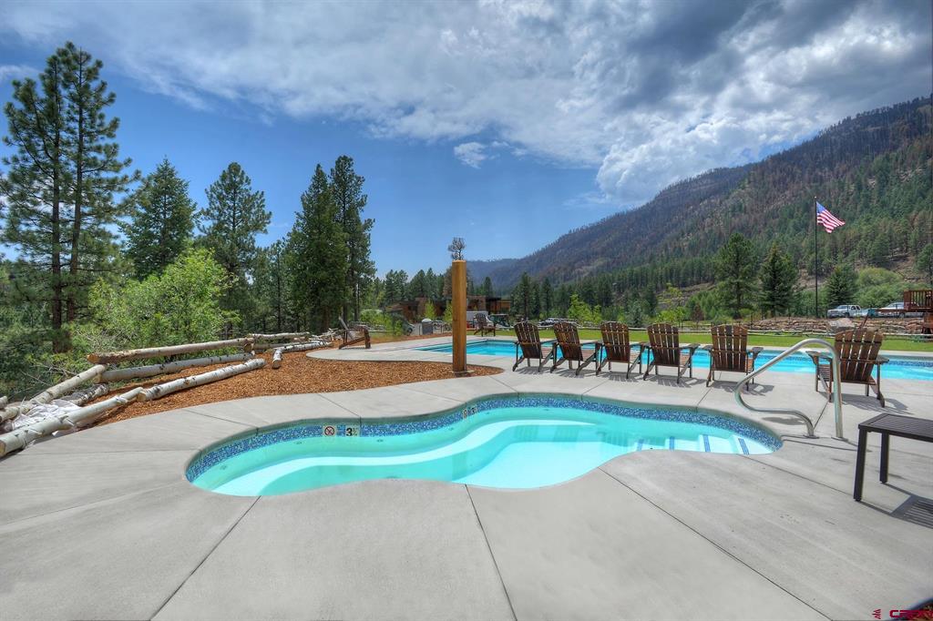 Outdoor pool and spa with lounge chairs, pine trees, and a mountain backdrop.