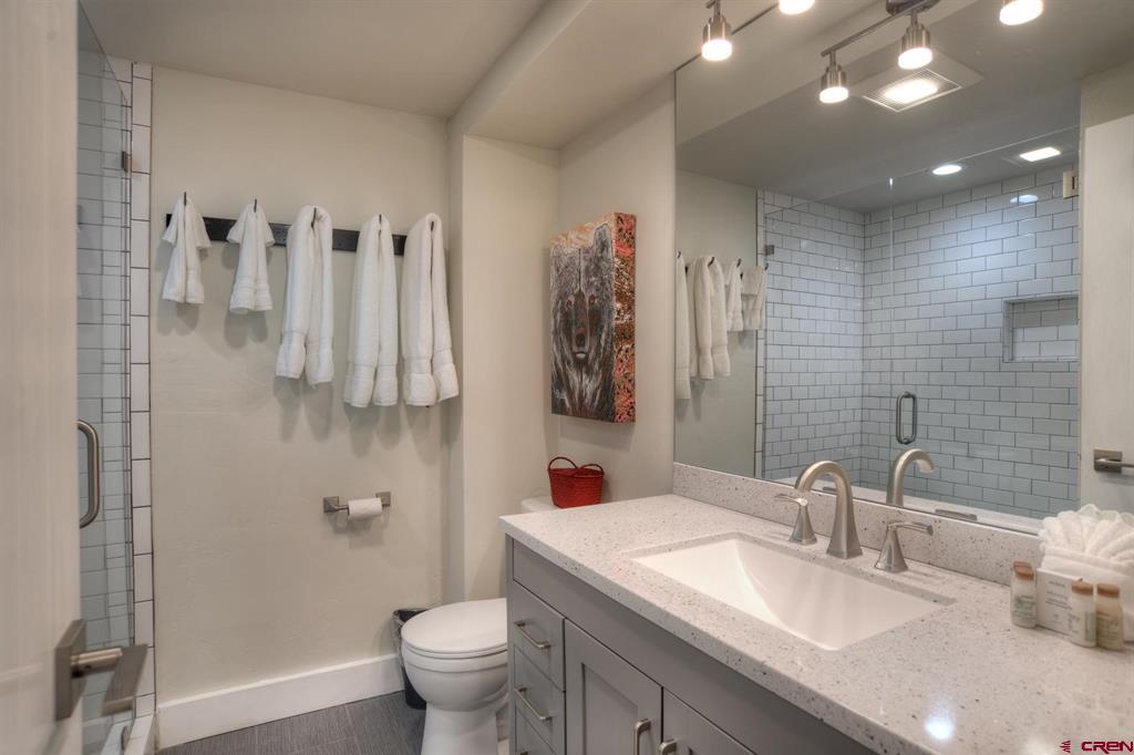 Bathroom with a gray vanity, large mirror, white subway-tile shower, and towels on wall hooks.