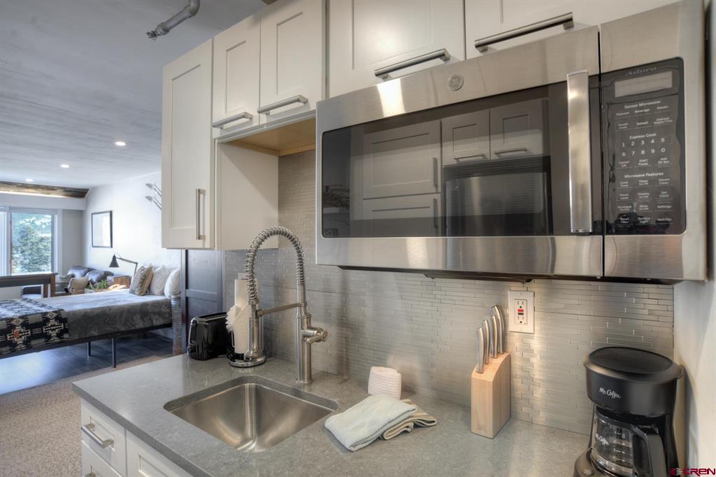 Condo kitchenette with stainless microwave and spring-coil faucet, opening onto a sleeping area.