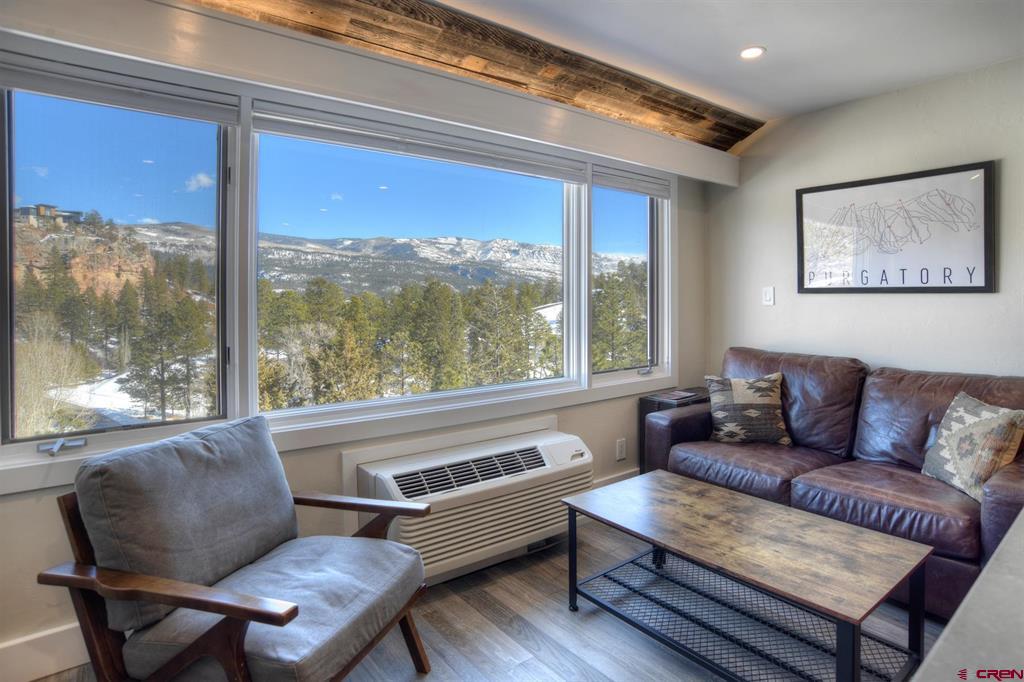 Living room with leather seating and large windows overlooking snow-dusted mountains and pine trees.