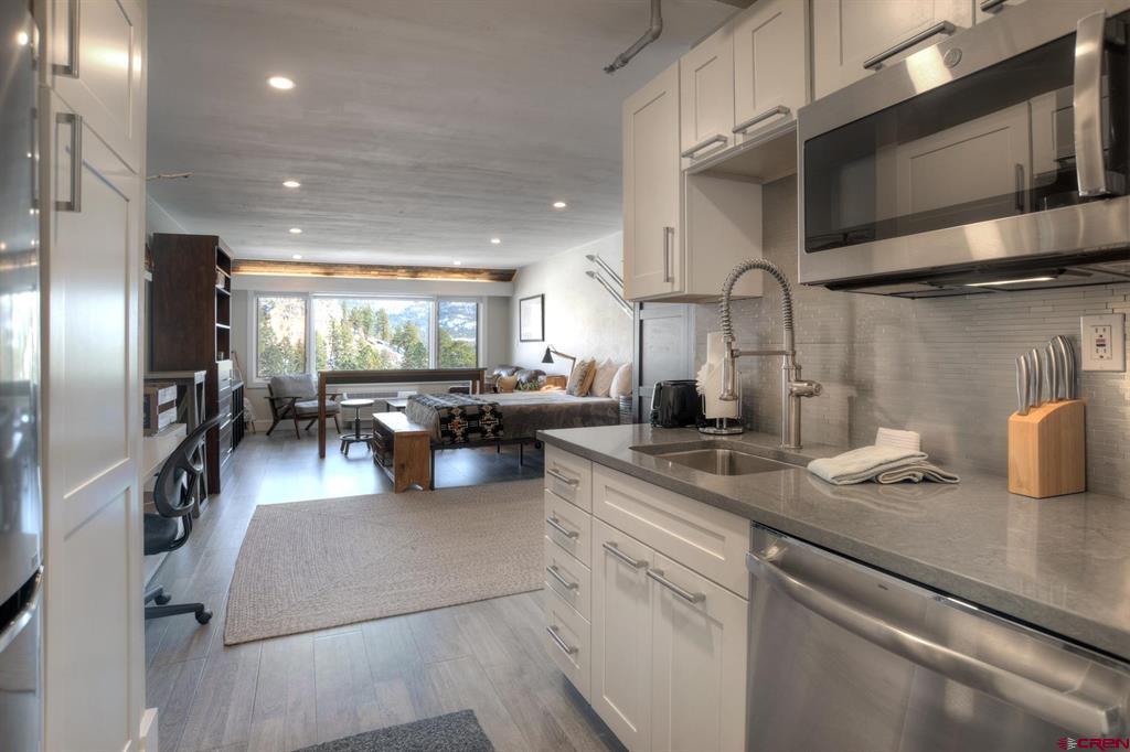 Condo kitchen opens into a furnished living and sleeping area with large windows and a mountain view.