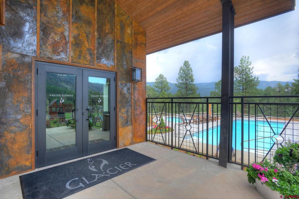 Covered fitness-center entrance beside a blue outdoor pool, with pine trees and mountain ridges beyond.