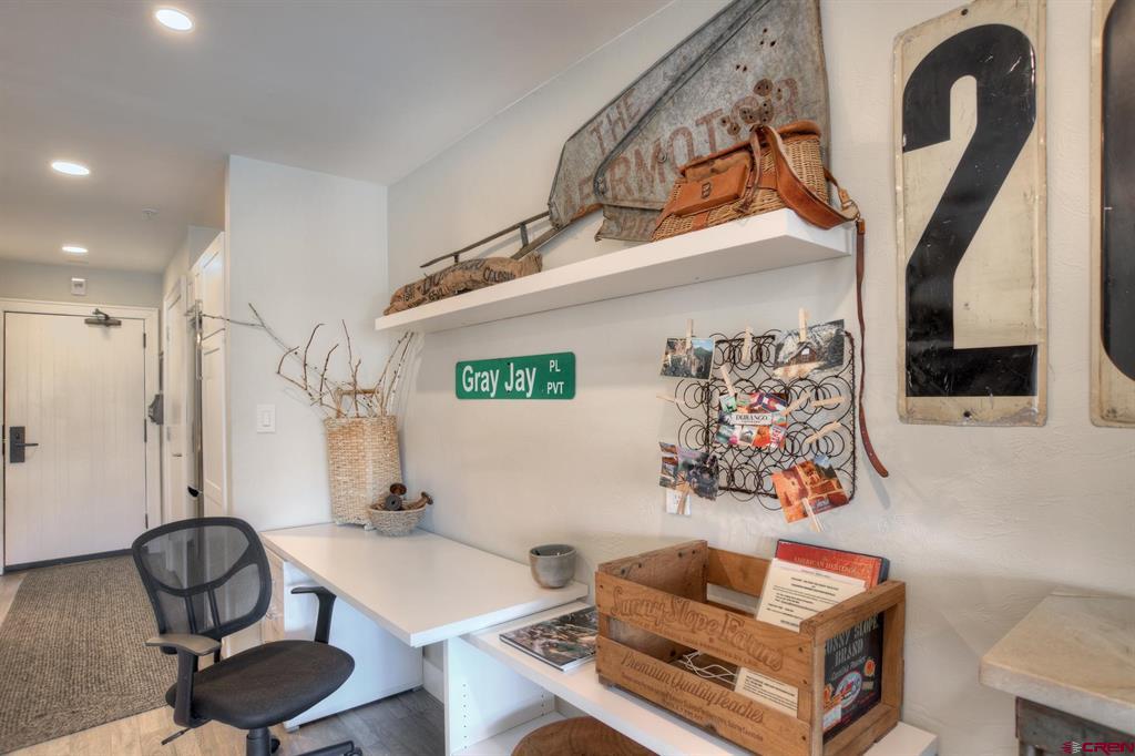 Office nook with a white desk, black mesh chair, and wall display shelf.