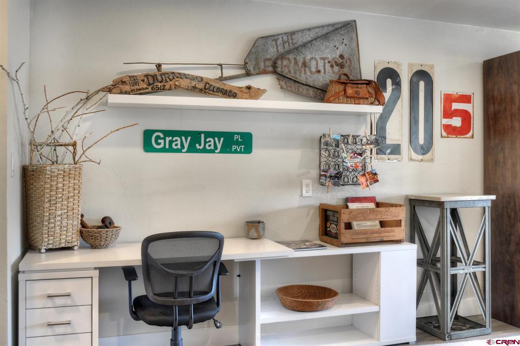 Home office nook with a white desk, black mesh chair, and vintage Colorado street-sign decor.