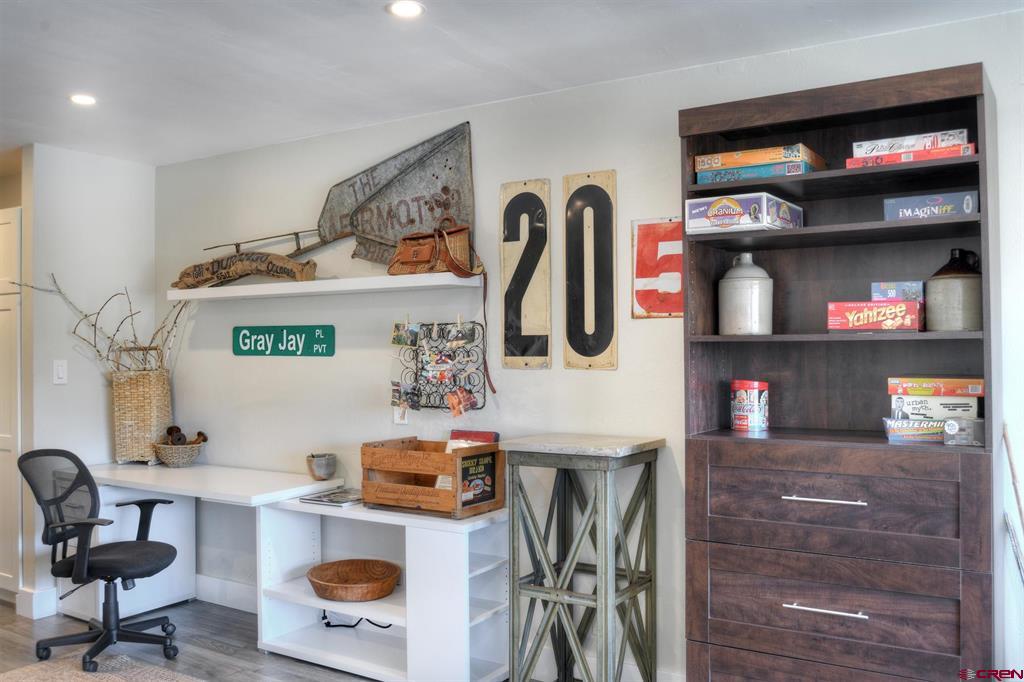 Furnished home office with a white desk, black chair, and dark wood bookcase filled with board games.
