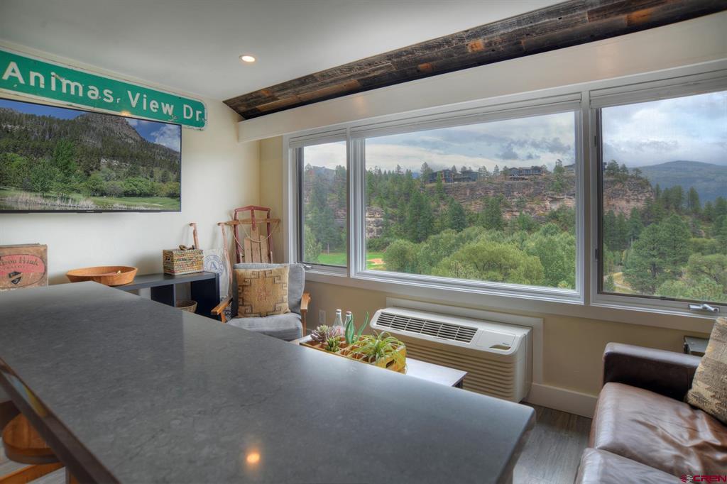 Condo sitting area with wide windows overlooking wooded cliffs and mountains, viewed over a dark countertop.