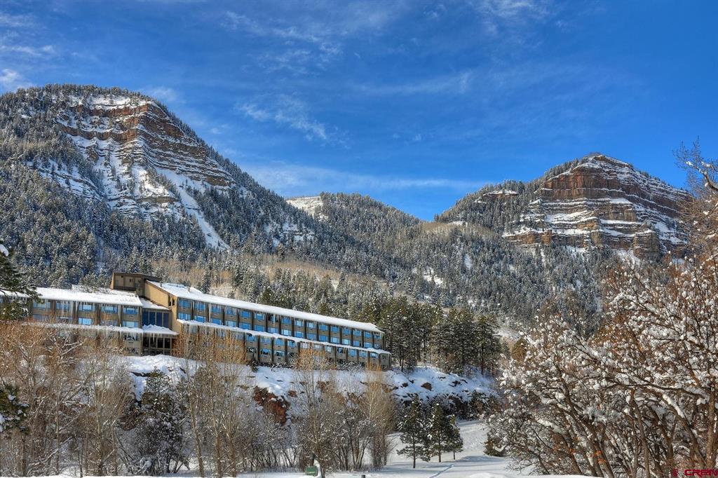 Mountain lodging building below snow-covered cliffs and forested slopes.
