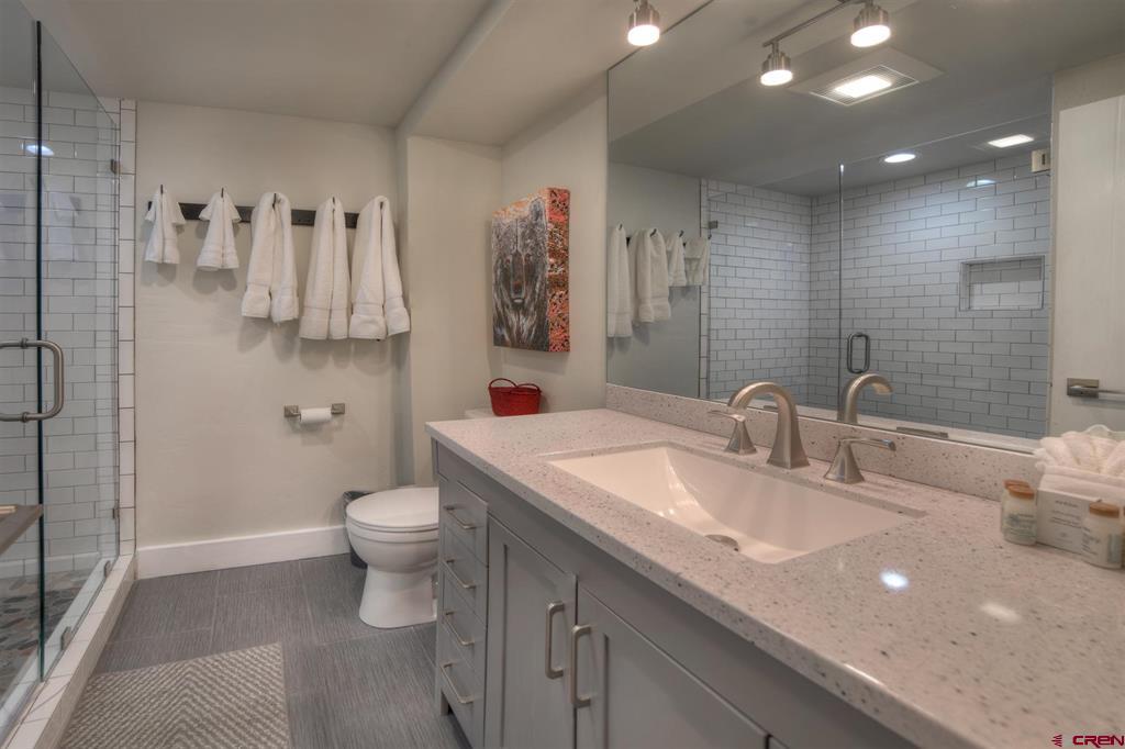 Bathroom with a double-sink vanity and glass shower lined with white subway tile.